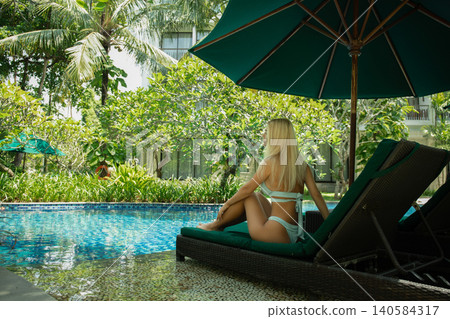 Woman enjoys tranquility by the poolside in a lush garden 140584317
