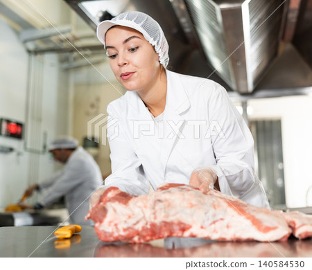Female butcher preparing raw pork ribs for sale in butchery 140584530