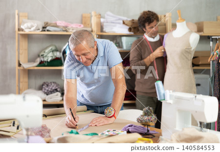 mature man draws clothes on paper against the background of an assistant 140584553
