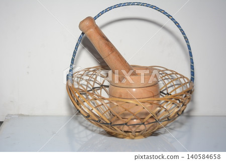 Small wooden mortar and pestle inside an empty woven wicker basket with handmade Small wooden mortar and pestle inside an empty woven wicker basket with handmade 140584658