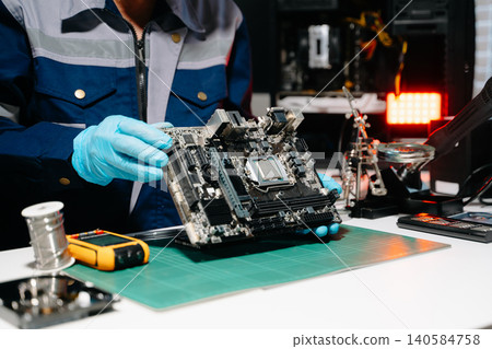 Professional senior technician holding and inspecting computer motherboard at high-tech electronics repair workstation 140584758