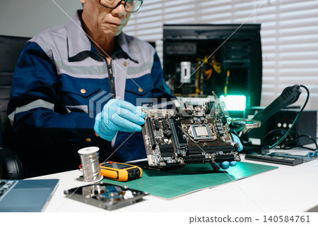 Professional senior technician holding and inspecting computer motherboard at high-tech electronics repair workstation 140584761