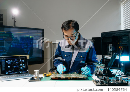 Professional senior technician holding and inspecting computer motherboard at high-tech electronics repair workstation 140584764