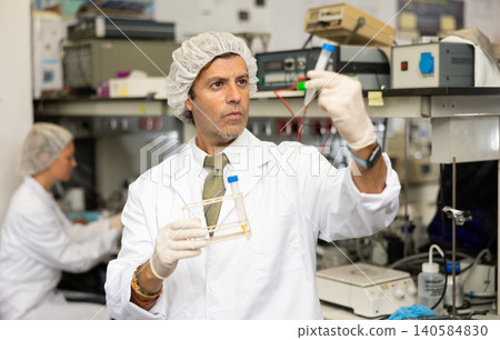 Serious Latin male biochemist holding tripod and examining solution in test tube for chemical reaction in research center Serious Latin male biochemist holding tripod and examining solution in test tube for chemical reaction in research center 140584830