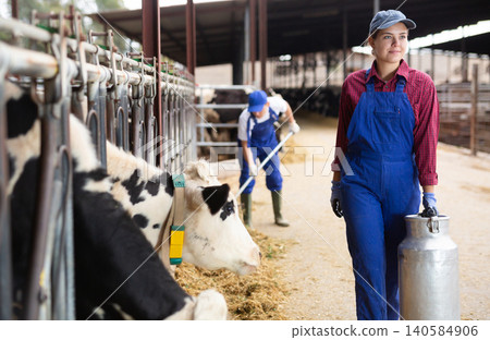 Female owner with milk can standing in stall on background with herd of cows Female owner with milk can standing in stall on background with herd of cows 140584906