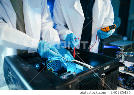 Engineers testing computer hardware with multimeter inside technology laboratory. Electronics repair, motherboard diagnostics Engineers testing computer hardware with multimeter inside technology laboratory. Electronics repair, motherboard diagnostics 140585425