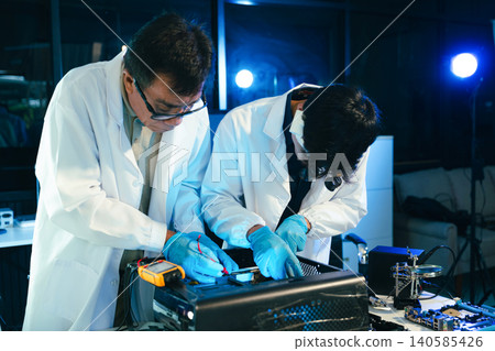 Engineers testing computer hardware with multimeter inside technology laboratory. Electronics repair, motherboard diagnostics Engineers testing computer hardware with multimeter inside technology laboratory. Electronics repair, motherboard diagnostics 140585426