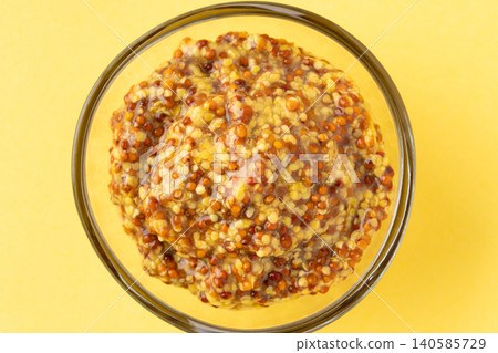 Close-up of whole-grain mustard in a small dish against a yellow background. Close-up of whole-grain mustard in a small dish against a yellow background. 140585729