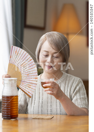 A senior woman pours herself some barley tea and drinks it in the living room. A senior woman pours herself some barley tea and drinks it in the living room. 140585847