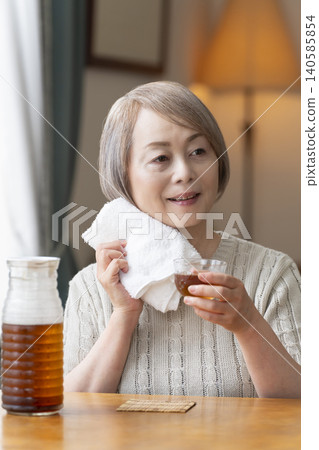 A senior woman pours herself some barley tea and drinks it in the living room. 140585854