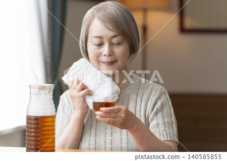 A senior woman pours herself some barley tea and drinks it in the living room. A senior woman pours herself some barley tea and drinks it in the living room. 140585855