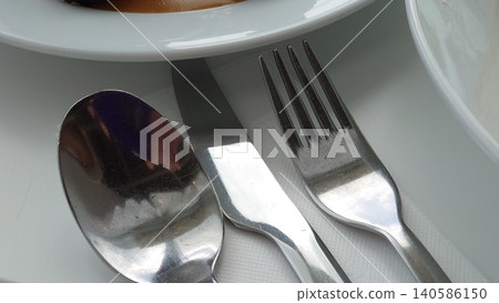 Metal spoons, knives, and forks are neatly arranged on a white table. Metal spoons, knives, and forks are neatly arranged on a white table. 140586150