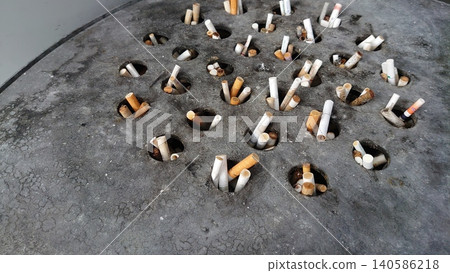 Numerous cigarette butts were stuck into the holes of an outdoor concrete ashtray. 140586218