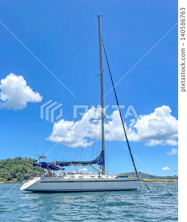 White sailboat with blue sails glides across the sparkling blue ocean under a cloudy sky White sailboat with blue sails glides across the sparkling blue ocean under a cloudy sky 140586763