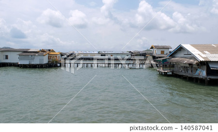 Traditional stilt buildings constructed over calm sea water near Ban Phe Pier with cloudy sky in background. Coastal architecture concept Traditional stilt buildings constructed over calm sea water near Ban Phe Pier with cloudy sky in background. Coastal architecture concept 140587041