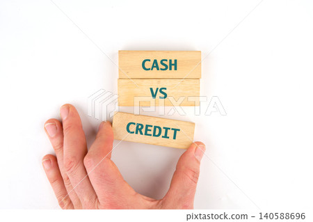 A hand holds wooden blocks with the words cash and credit written on them. This shows a comparison of payment methods. The setting is bright and simple A hand holds wooden blocks with the words cash and credit written on them. This shows a comparison of payment methods. The setting is bright and simple 140588696