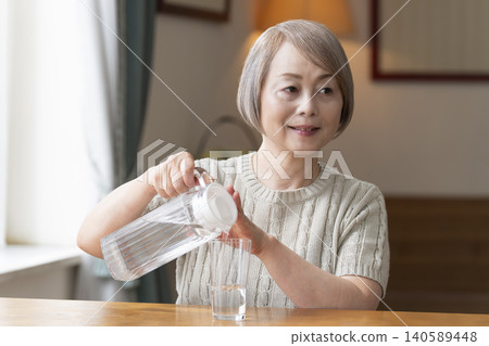 Senior woman drinks water in the living room to prevent heatstroke Senior woman drinks water in the living room to prevent heatstroke 140589448