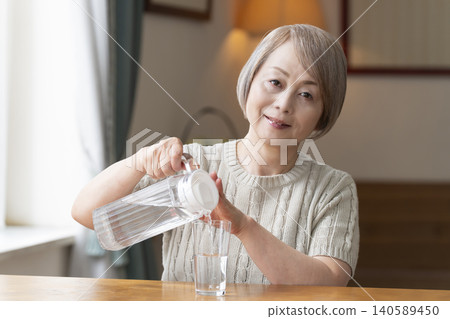 Senior woman drinks water in the living room to prevent heatstroke Senior woman drinks water in the living room to prevent heatstroke 140589450