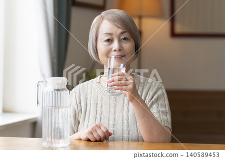Senior woman drinks water in the living room to prevent heatstroke Senior woman drinks water in the living room to prevent heatstroke 140589453
