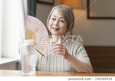Senior woman drinks water in the living room to prevent heatstroke Senior woman drinks water in the living room to prevent heatstroke 140589456
