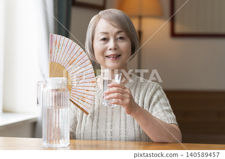 Senior woman drinks water in the living room to prevent heatstroke Senior woman drinks water in the living room to prevent heatstroke 140589457