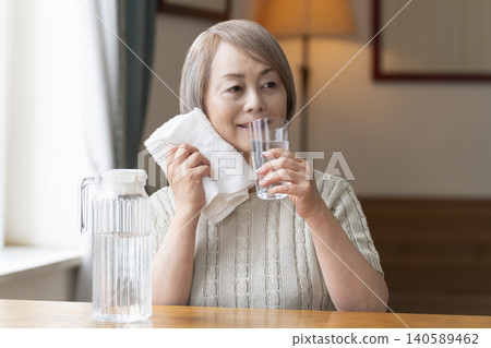 Senior woman drinks water in the living room to prevent heatstroke Senior woman drinks water in the living room to prevent heatstroke 140589462