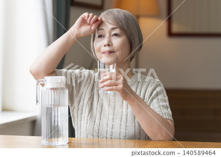 老年婦女在客廳喝水以預防中暑 老年婦女在客廳喝水以預防中暑 140589464