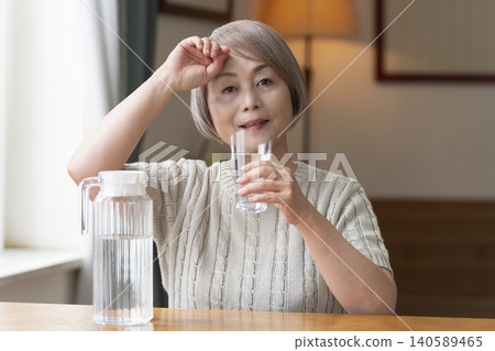 Senior woman drinks water in the living room to prevent heatstroke Senior woman drinks water in the living room to prevent heatstroke 140589465