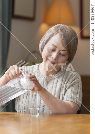 Senior woman drinks water in the living room to prevent heatstroke Senior woman drinks water in the living room to prevent heatstroke 140589467