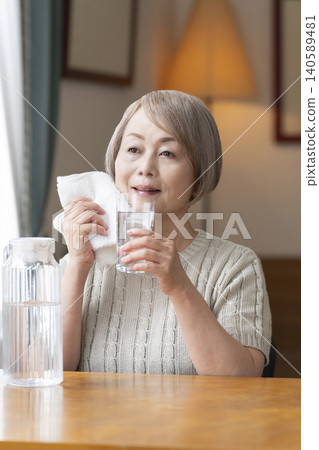 老年婦女在客廳喝水以預防中暑 老年婦女在客廳喝水以預防中暑 140589481