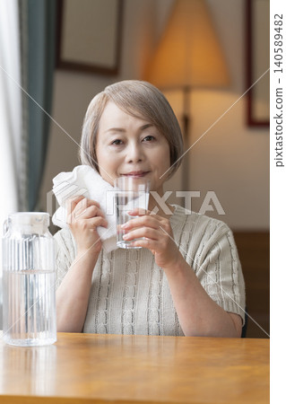 Senior woman drinks water in the living room to prevent heatstroke Senior woman drinks water in the living room to prevent heatstroke 140589482