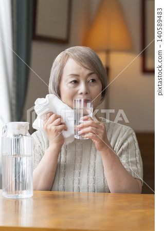 老年婦女在客廳喝水以預防中暑 老年婦女在客廳喝水以預防中暑 140589483