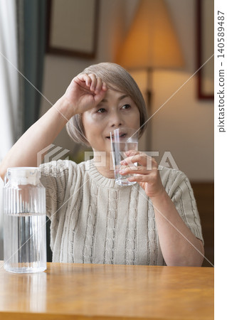 Senior woman drinks water in the living room to prevent heatstroke Senior woman drinks water in the living room to prevent heatstroke 140589487