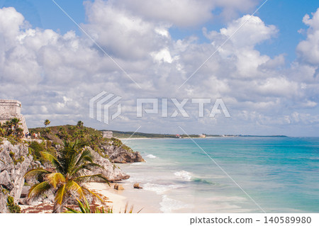 Tulum Mayan ruins overlooking a Caribbean beach with turquoise sea, ancient civilization architecture on a rock cliff, and lush tropical vegetation under a cloudy sky, ideal vacation destination Tulum Mayan ruins overlooking a Caribbean beach with turquoise sea, ancient civilization architecture on a rock cliff, and lush tropical vegetation under a cloudy sky, ideal vacation destination 140589980