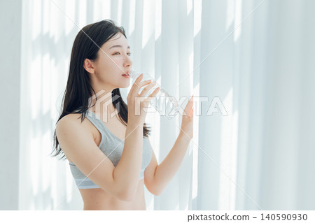 Woman drinking water by the window Woman drinking water by the window 140590930