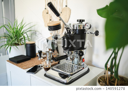 Home barista station with manual lever espresso machine, single dose grinder, and a smartphone on the counter. Home barista station with manual lever espresso machine, single dose grinder, and a smartphone on the counter. 140591278