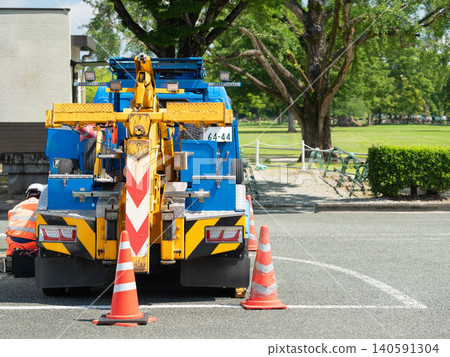 Tow truck or breakdown service vehicle with safety orange cones parked outdoor near a park. 140591304