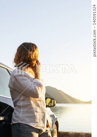 Woman traveler with smartphone next to parked car. Sea with mountains in the background. Woman traveler with smartphone next to parked car. Sea with mountains in the background. 140591324