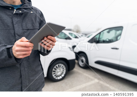 Fleet manager with digital tablet supervising rows of white delivery vans 140591395