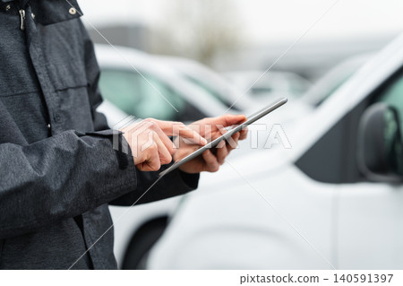 Fleet manager with digital tablet supervising rows of white delivery vans 140591397