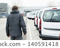 Fleet manager with digital tablet supervising rows of white delivery vans. 140591418