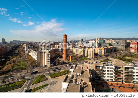Aerial view of Barcelona showcasing urban architecture, including residential buildings and the iconic red brick tower. Clear blue sky enhances the vibrant cityscape. Aerial view of Barcelona showcasing urban architecture, including residential buildings and the iconic red brick tower. Clear blue sky enhances the vibrant cityscape. 140592129