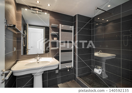 Modern bathroom with sleek black tiles, a white sink, and a glass shower. Bright lighting enhances the contemporary design. Modern bathroom with sleek black tiles, a white sink, and a glass shower. Bright lighting enhances the contemporary design. 140592135