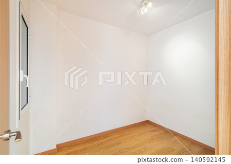 Empty room with white walls and wooden floor. A door is visible on the left side. The space is well-lit with a ceiling light. Empty room with white walls and wooden floor. A door is visible on the left side. The space is well-lit with a ceiling light. 140592145
