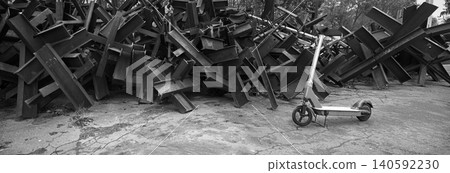 A scooter against the backdrop of iron anti-tank hedgehogs A scooter against the backdrop of iron anti-tank hedgehogs 140592230