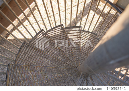 High angle looking down view of a modern industrial spiral staircase made of metal mesh steps. Geometric pattern created by steps and shadows in architectural photography style. Top down perspective High angle looking down view of a modern industrial spiral staircase made of metal mesh steps. Geometric pattern created by steps and shadows in architectural photography style. Top down perspective 140592341