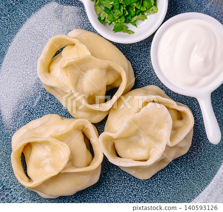 Hearty manti dumplings served with fresh herbs and creamy sour cream 140593126