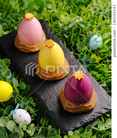 Colorful Easter egg desserts displayed on slate in green grass Colorful Easter egg desserts displayed on slate in green grass 140593141