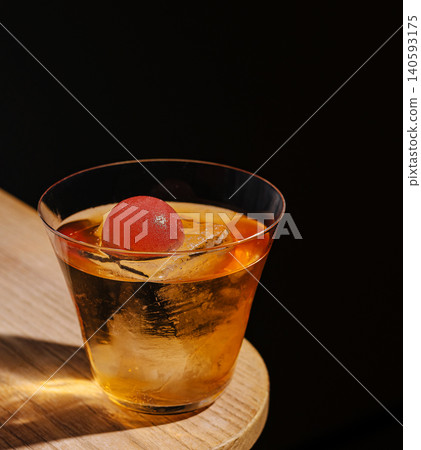 Amber cocktail with spherical red garnish on wooden surface 140593175