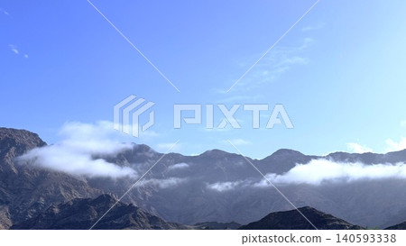 Mountain ridge with low clouds under clear blue sky Mountain ridge with low clouds under clear blue sky 140593338